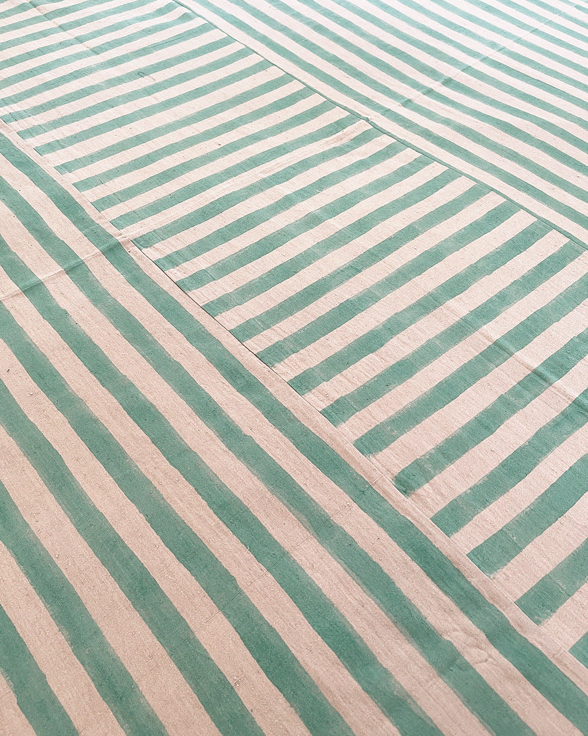 A handmade artisan blanket naturally dyed and handwoven with block-printed fabric in green and tan stripes.