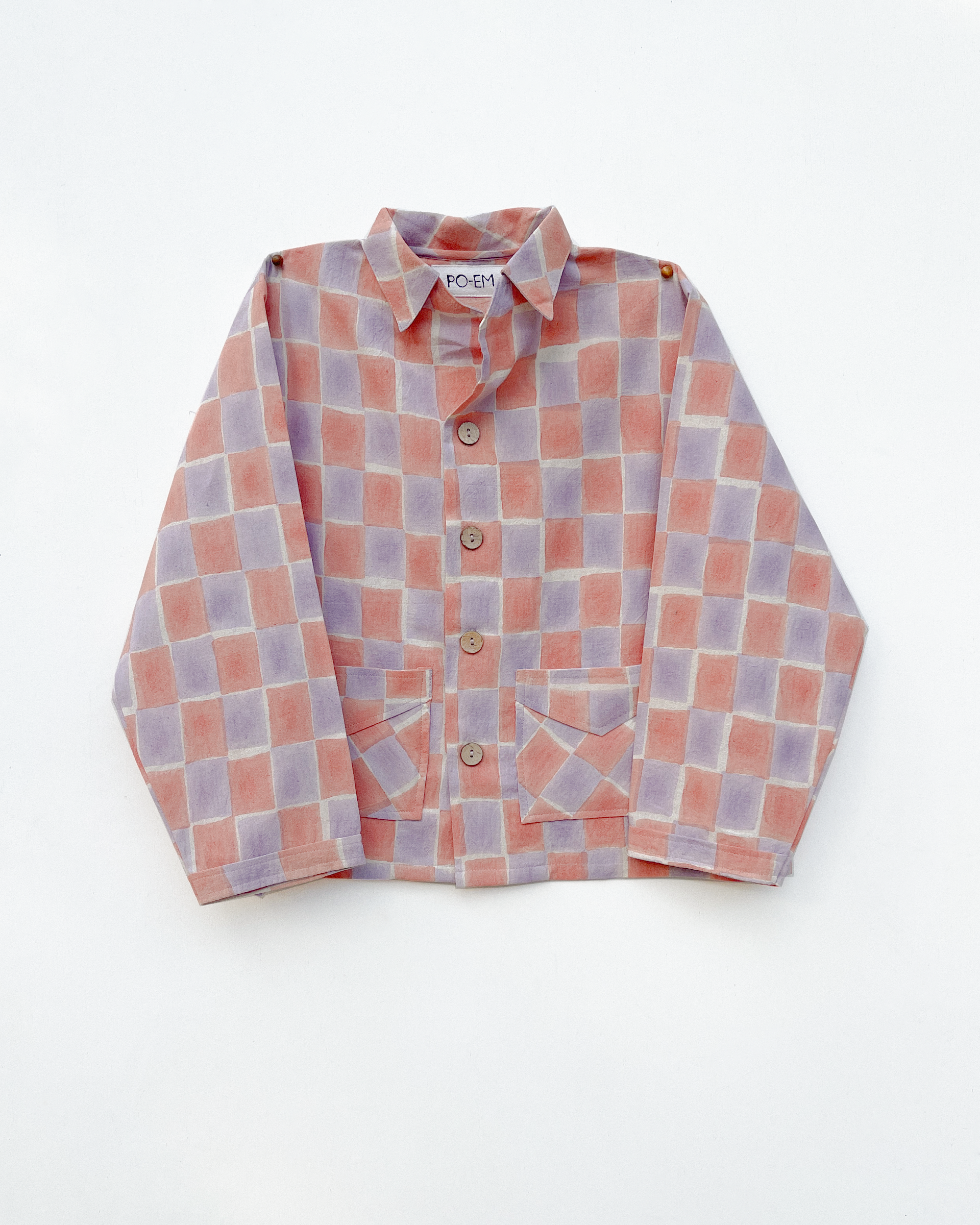Front view of the PO-EM Eli Jacket in Sala block-print. A boxy-cut, long-sleeved handloom cotton jacket featuring a layered checkerboard pattern in soft pink and lavender with coconut shell buttons.
