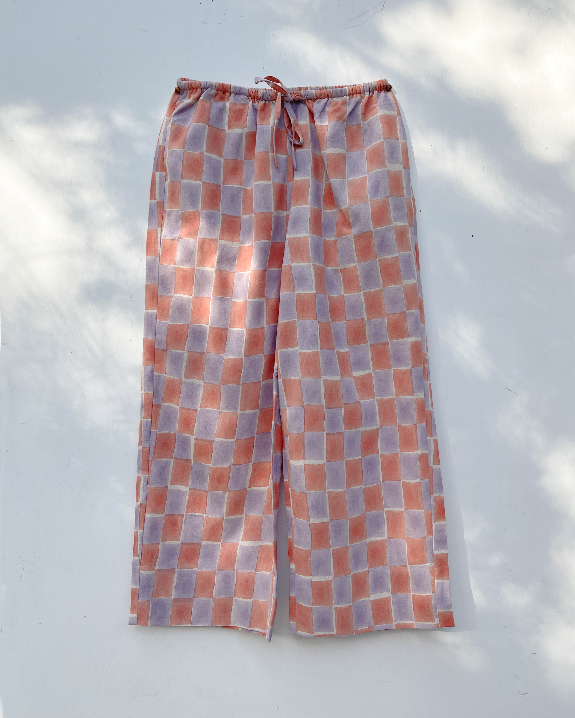 Full front view of the PO-EM Beachcomber Tie Pants in Sala block-print. Features a relaxed wide-leg silhouette in handwoven cotton with a layered pink and lavender checkered pattern.