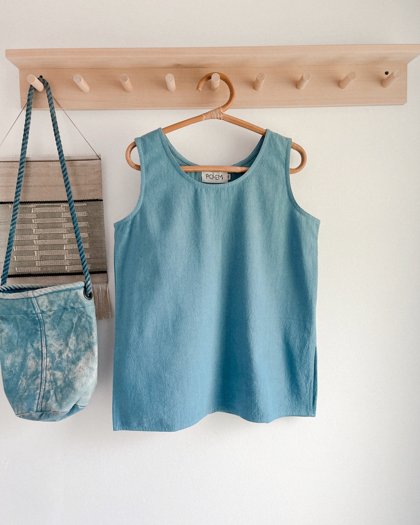 Blue tank top hanging on a wooden hanger against a white wall.