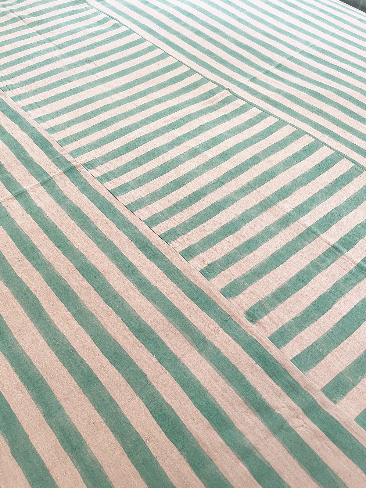 A handmade artisan blanket naturally dyed and handwoven with block-printed fabric in green and tan stripes.