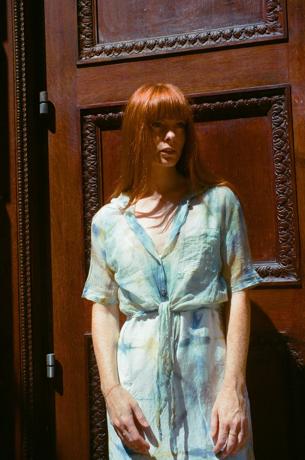 Woman in a tie-dye PO-EM Top and dress standing in front of a wooden door with intricate carvings in NYC. 