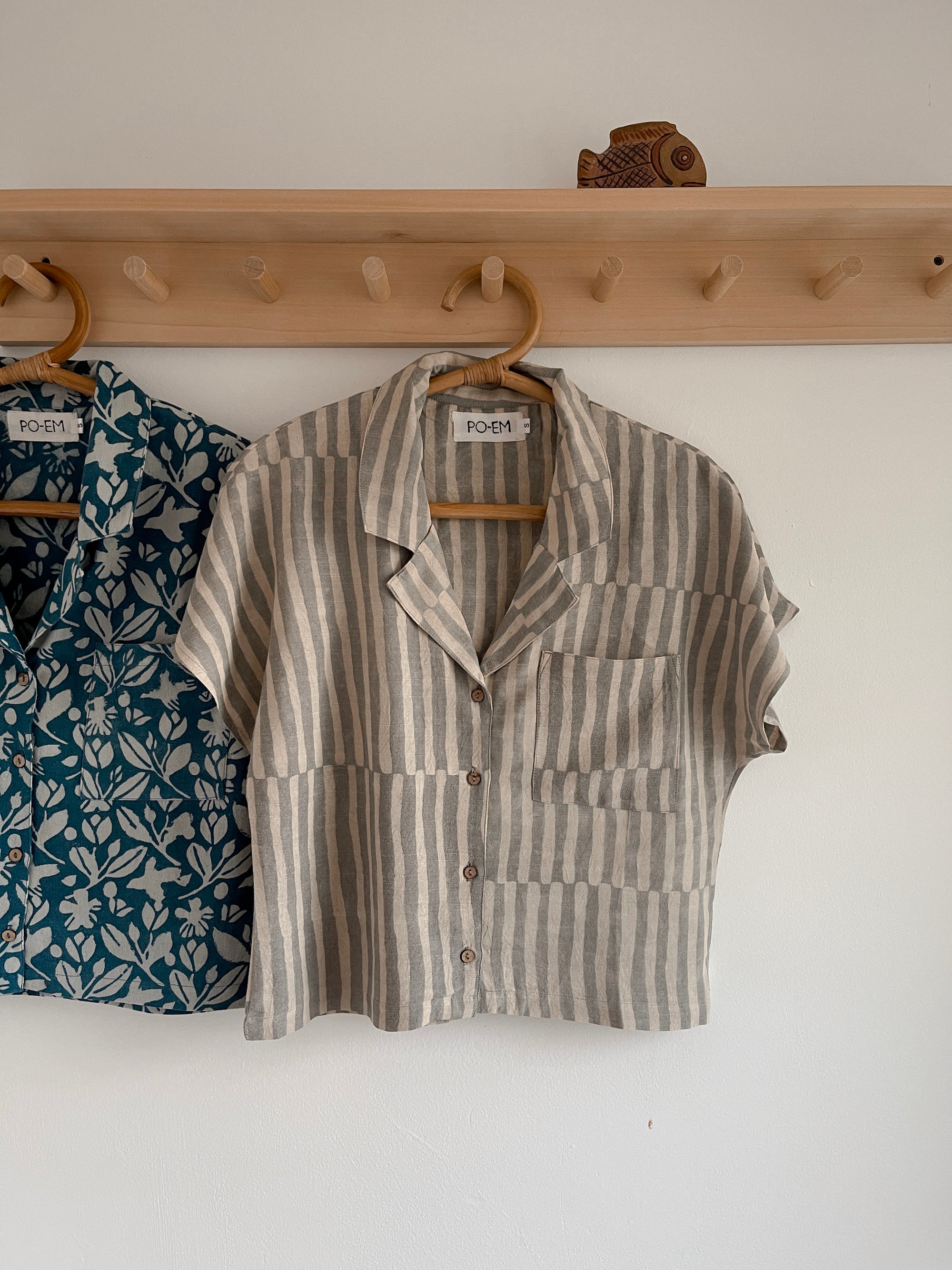 Striped shirt and floral dress hanging on a wooden rack against a white wall.